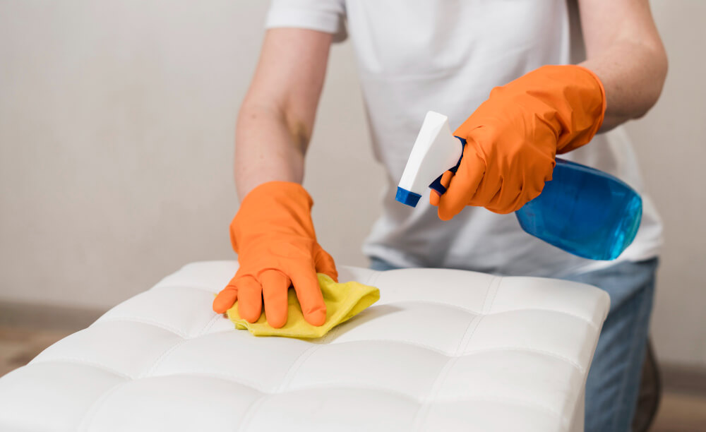 A person cleaning a mattress with disinfectant spray and cloth.