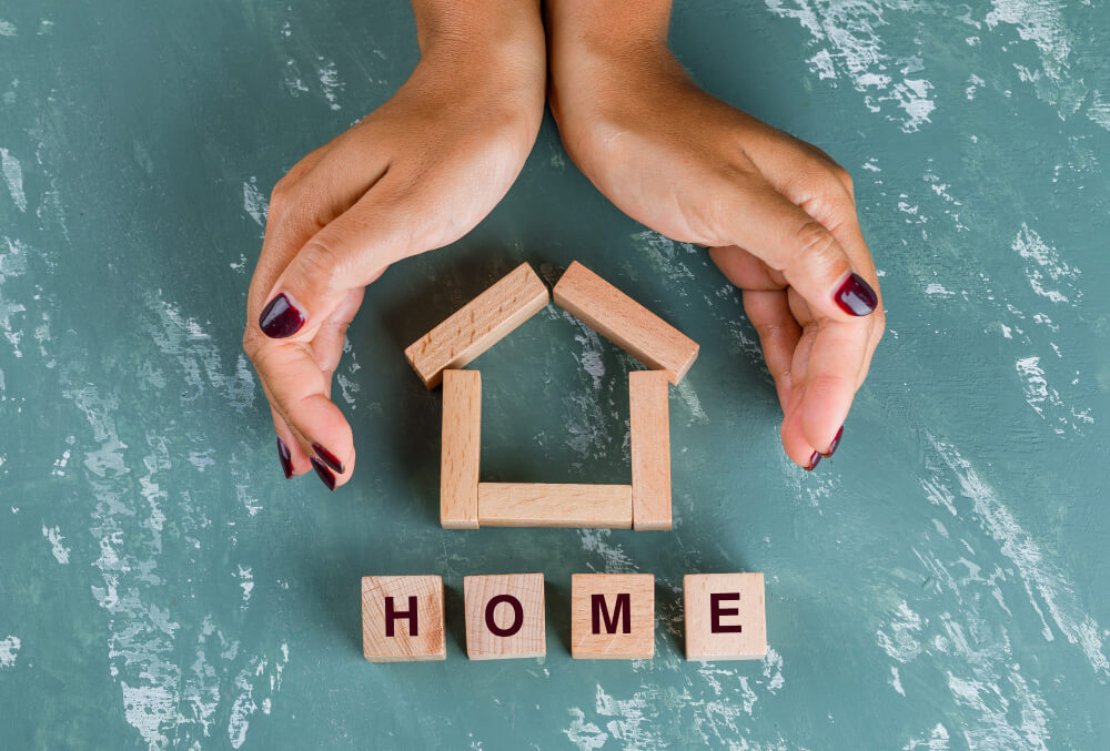Close-up of hands cradling a small wooden house with "HOME" written on it.